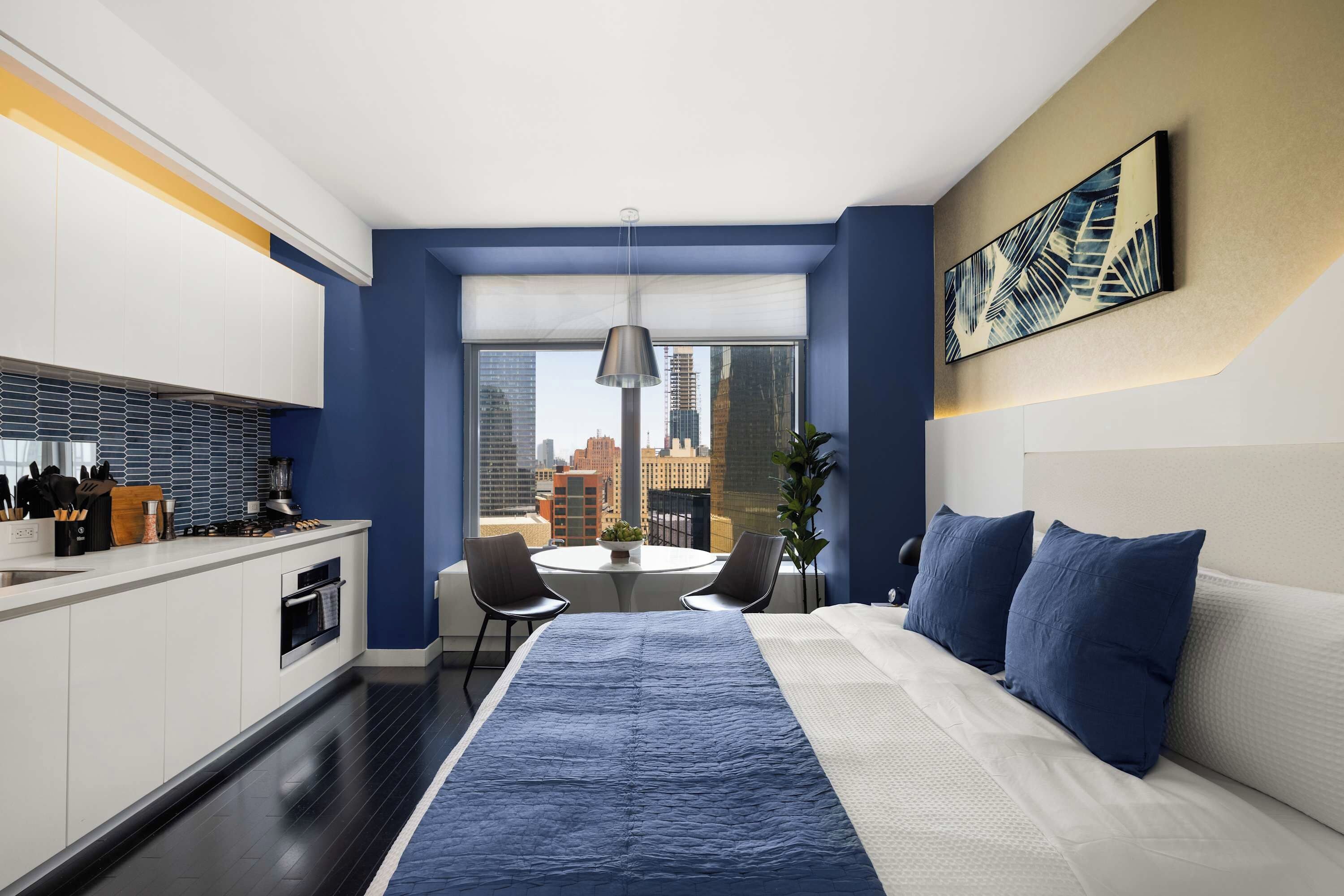 A modern hotel room with a large bed, a dining area, and a kitchen.