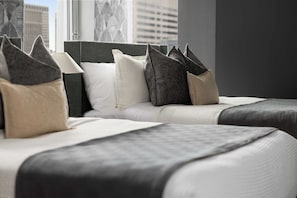 Ein Hotelzimmer mit einem großen Bett, vielen Kissen und Blick auf die Stadtlandschaft durch das Fenster.