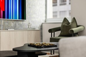 Een moderne woonkamer met een flatscreen televisie aan de muur, een bank met een opvallend kussendesign en een salontafel met een decoratieve metalen dienblad.