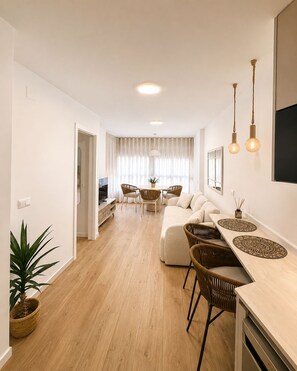 A modern living room with a sofa, dining table, and chairs. There is a TV, a potted plant, and a window with curtains. - A cozy and bright apartment, perfect for an unforgettable getaway (Torrox- costa)