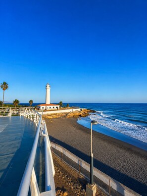 A coastal scene with a white lighthouse, a paved walkway, and a beach. - A cozy and bright apartment, perfect for an unforgettable getaway (Torrox- costa)