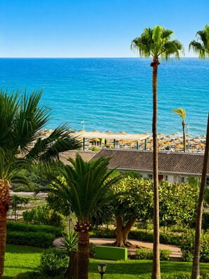 A coastal view with a beach, palm trees, and a building with a tiled roof. - A cozy and bright apartment, perfect for an unforgettable getaway (Torrox- costa)