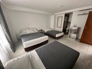 Ett hotellrum med två sängar, ett nattduksbord, en garderob och ett badrum som syns genom en öppen dörr.