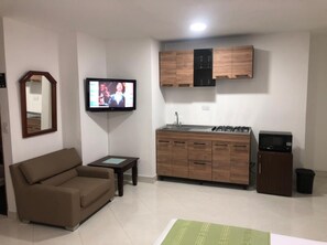 A compact living space with a sofa, a small table, a TV, a kitchenette with cabinets, a microwave, and a trash bin. - HOTEL FLORIDA INN (Medellín)