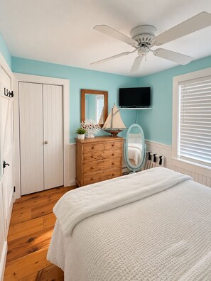 A bedroom with a bed, a dresser, a ceiling fan, a TV, and a window with blinds. - A Storybook Cape Cod Cottage by the Sea (Mashpee)