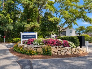 A private beach community sign, a stone flower bed, and a residential house. - A Storybook Cape Cod Cottage by the Sea (Mashpee)