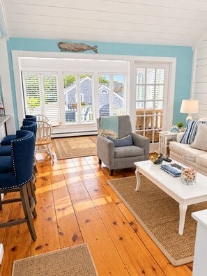 A living room with a wooden floor, a gray armchair, a white sofa, and a coffee table. - A Storybook Cape Cod Cottage by the Sea (Mashpee)