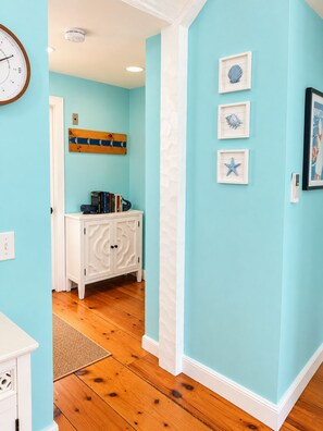 A hallway with a white cabinet, a clock, and framed pictures on the wall. - A Storybook Cape Cod Cottage by the Sea (Mashpee)