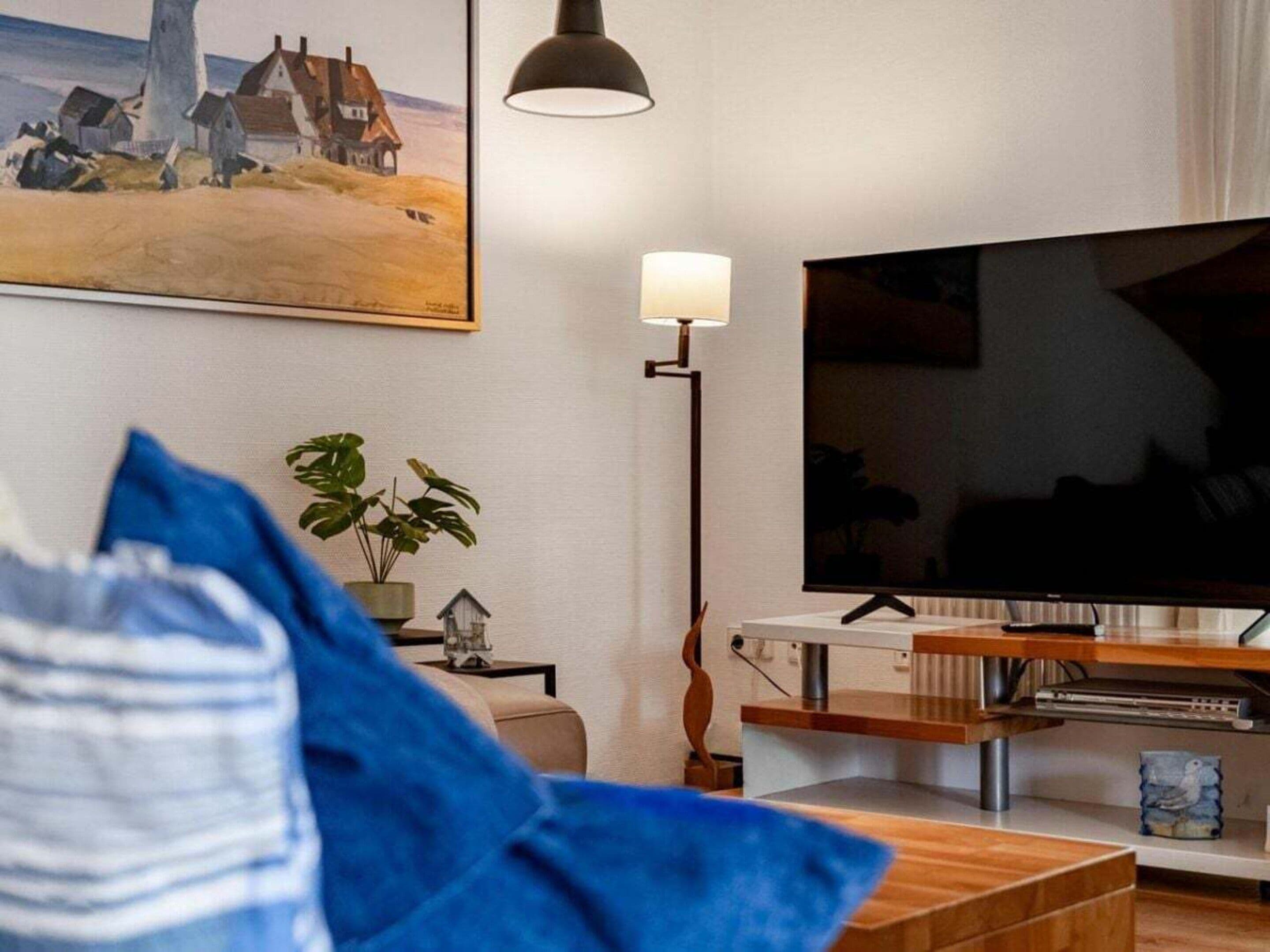 A living room with a television, a lamp, a painting, and a plant.