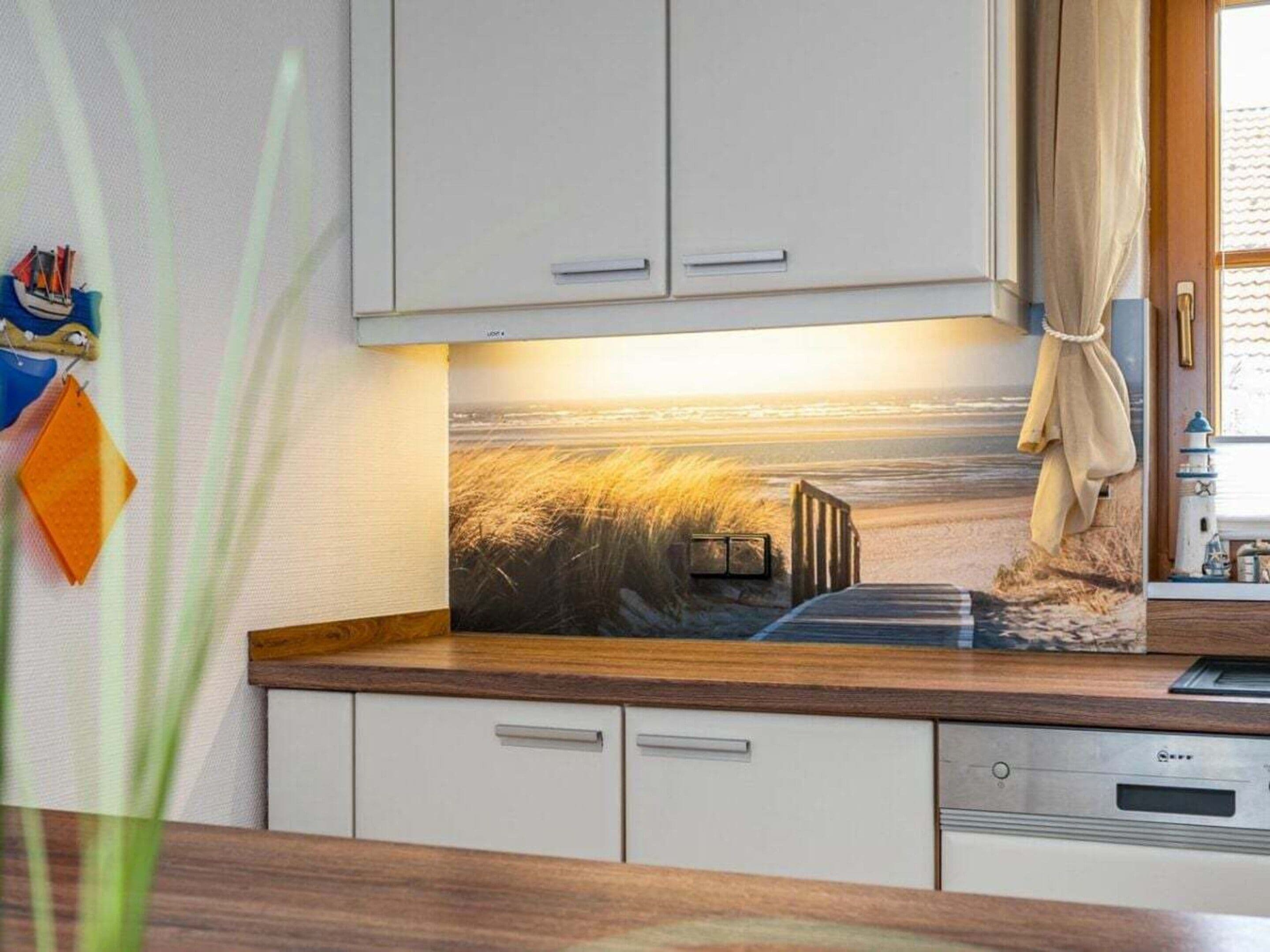 Cocina con armarios blancos, encimera de madera y un mural con paisaje costero.