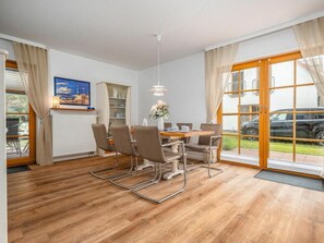 A dining area with a table and chairs, a radiator, a bookshelf, and a window with curtains. - 9a/t6 Holiday Home Park \"freesenbruch\" (Zingst)