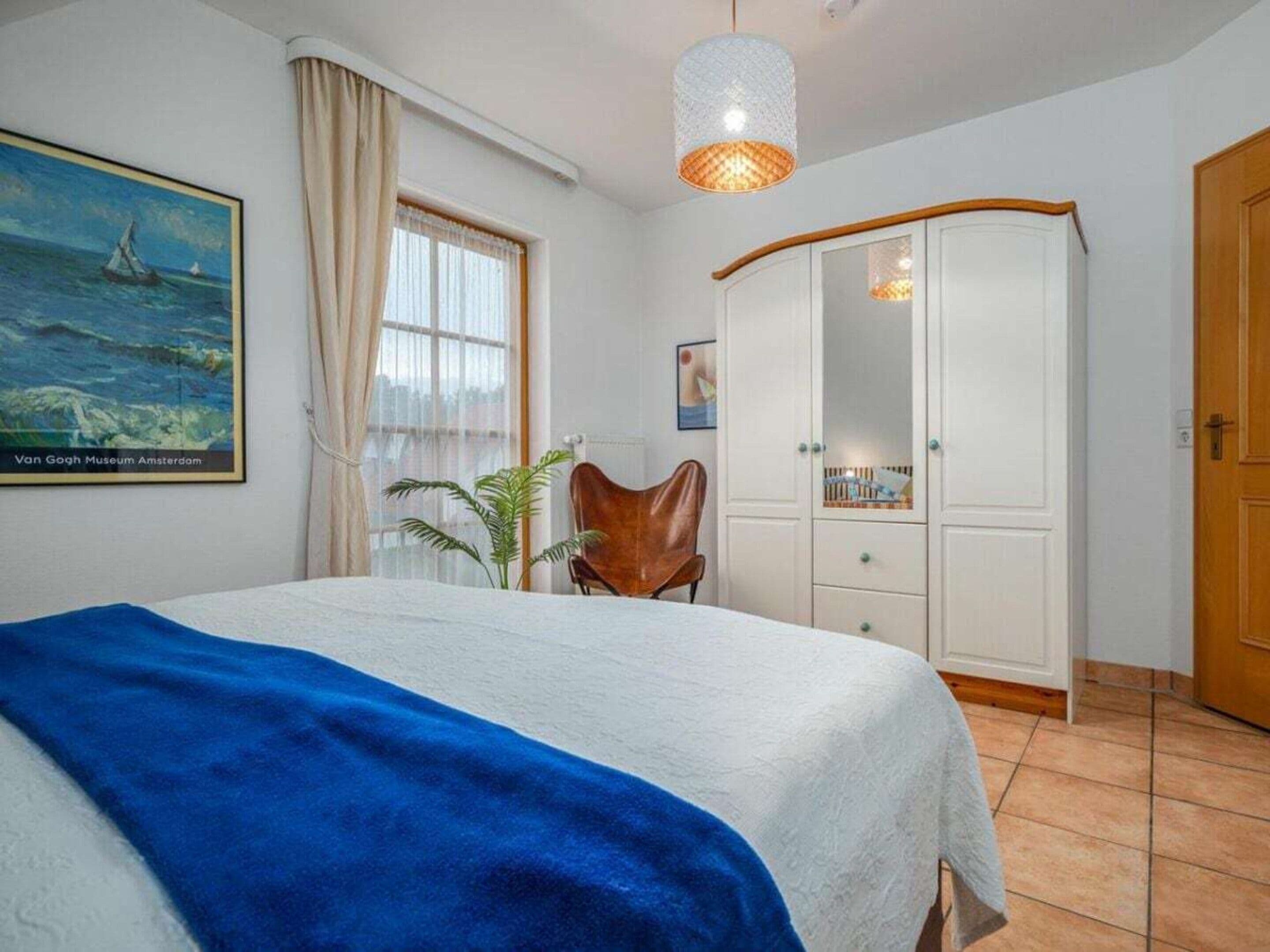 A bedroom with a bed, a wardrobe, a chair, a hanging light fixture, and a painting on the wall.