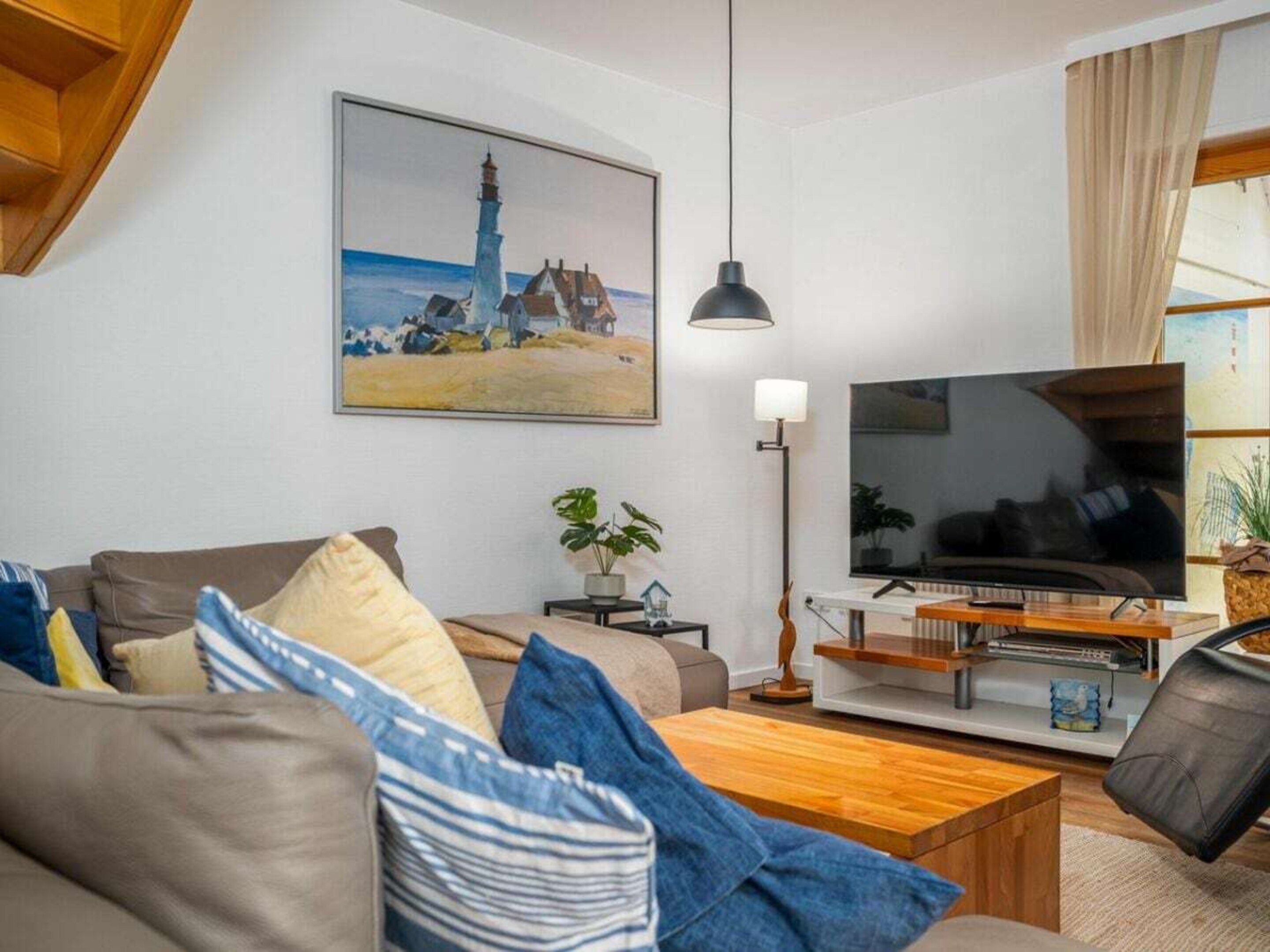 Un salon comprenant un canapé, une table basse, un téléviseur et un tableau représentant un phare.