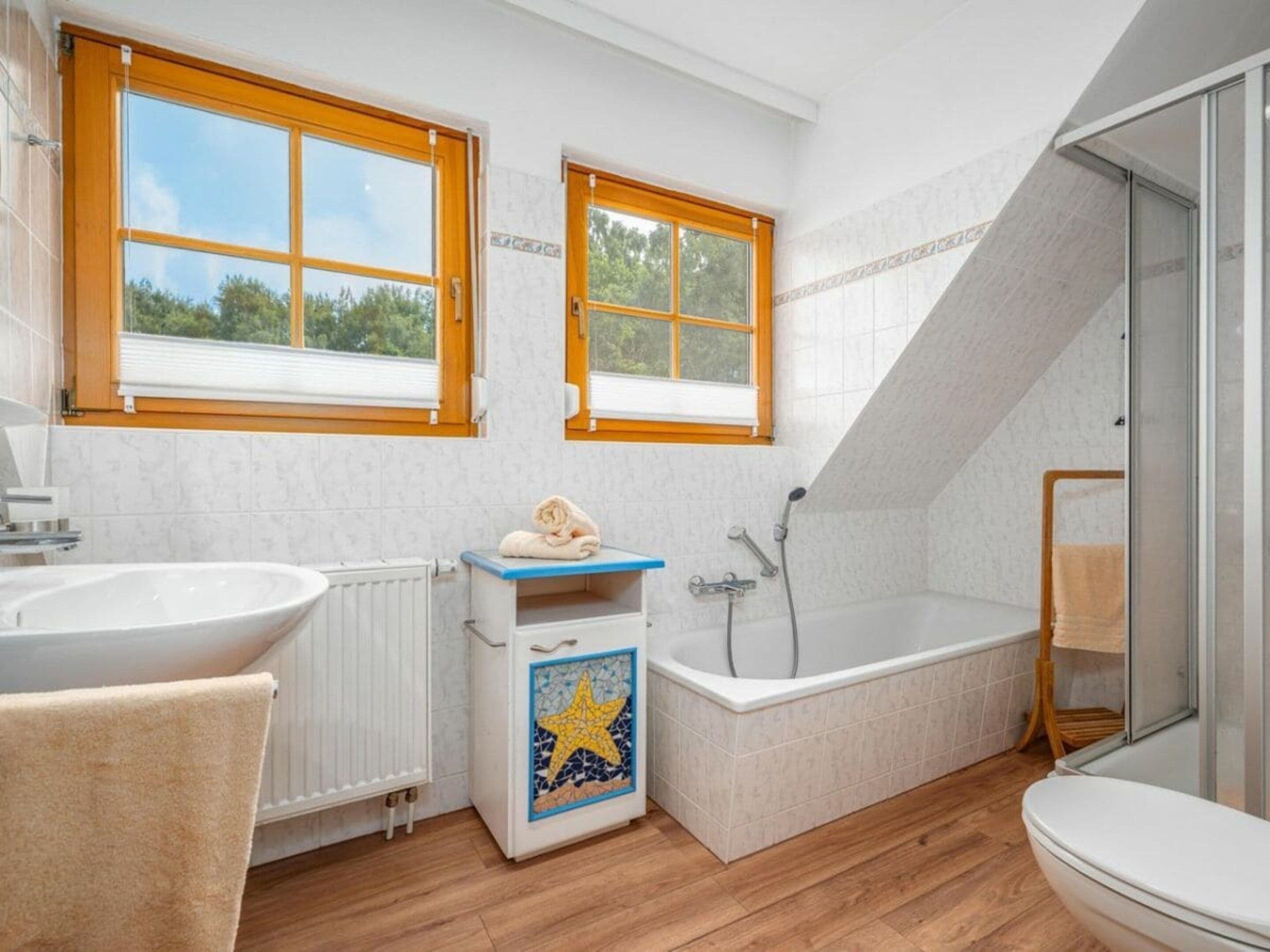Ett modernt badrum med badkar, handfat och toalett. Det finns två fönster med träramar.