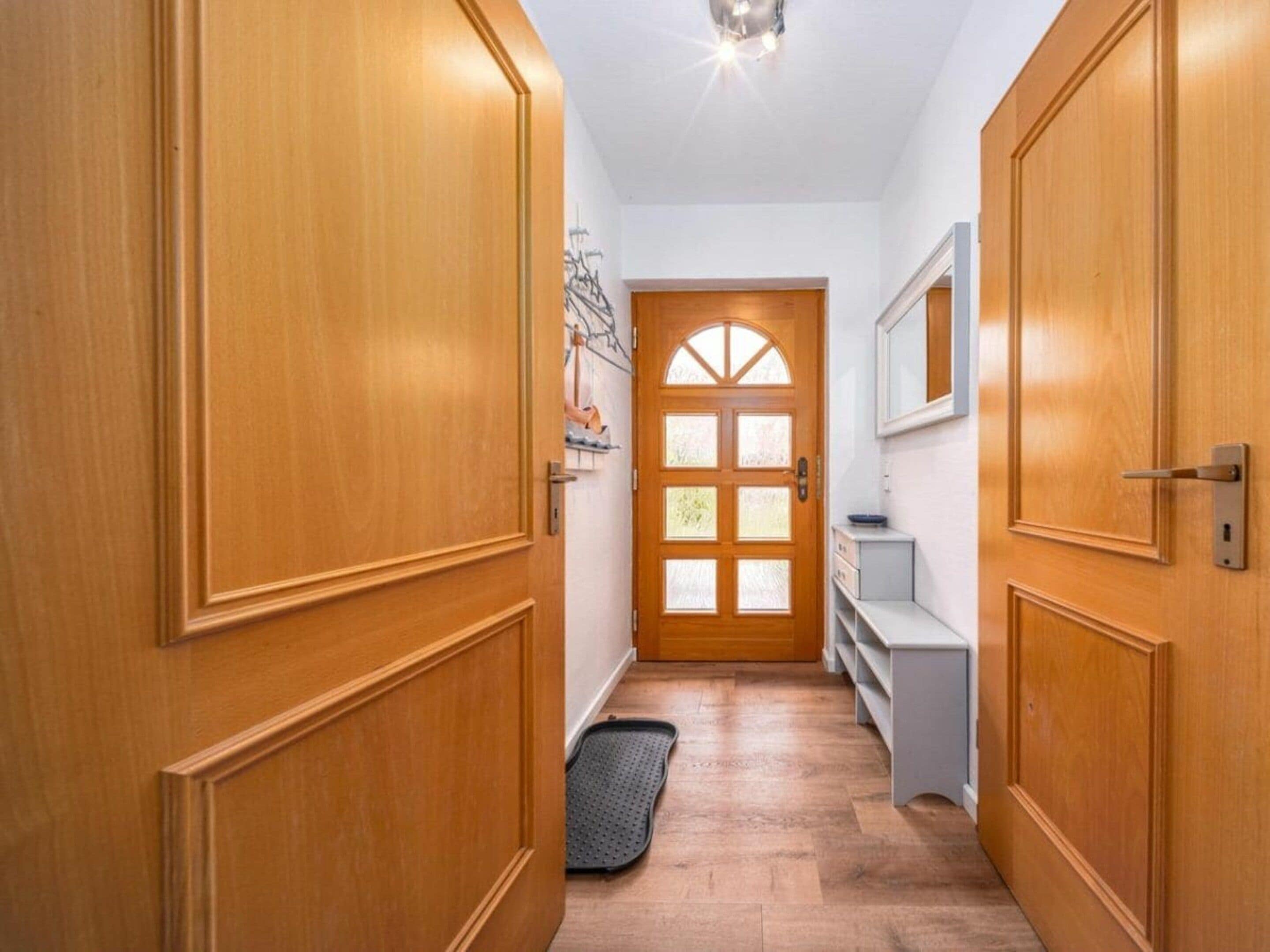 Ein Flur mit Holztüren, einer weißen Wand, einer Glastür und einer kleinen weißen Bank.