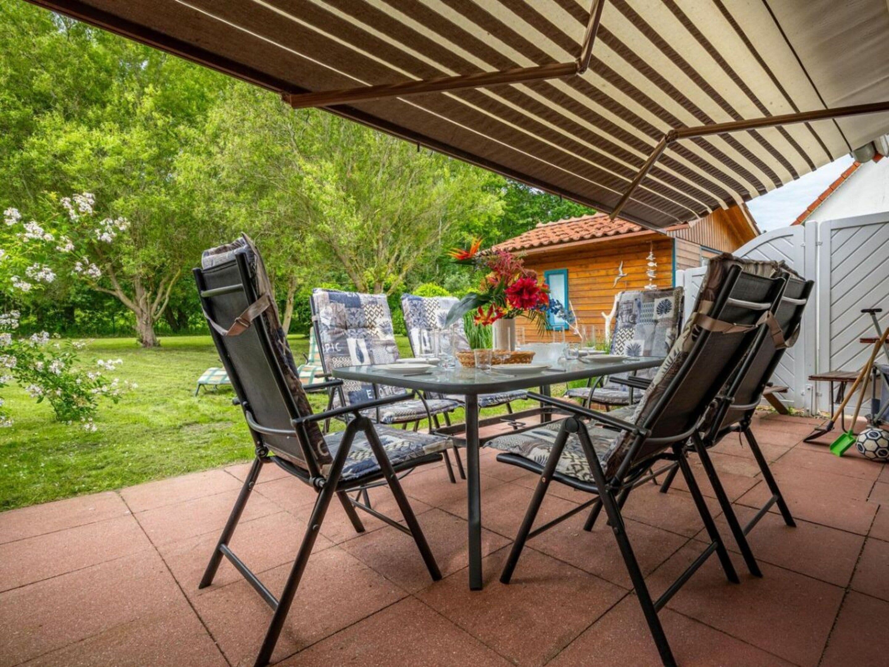 An outdoor patio with a table and chairs, surrounded by a garden and a wooden structure.