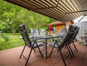An outdoor patio with a table and chairs, surrounded by a garden and a wooden structure. - 9a/t6 Holiday Home Park \"freesenbruch\" (Zingst)
