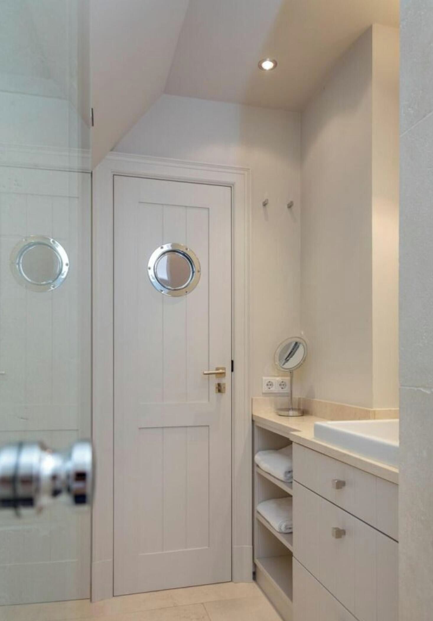 A bathroom with a white door, a round mirror, a sink, and a towel shelf.