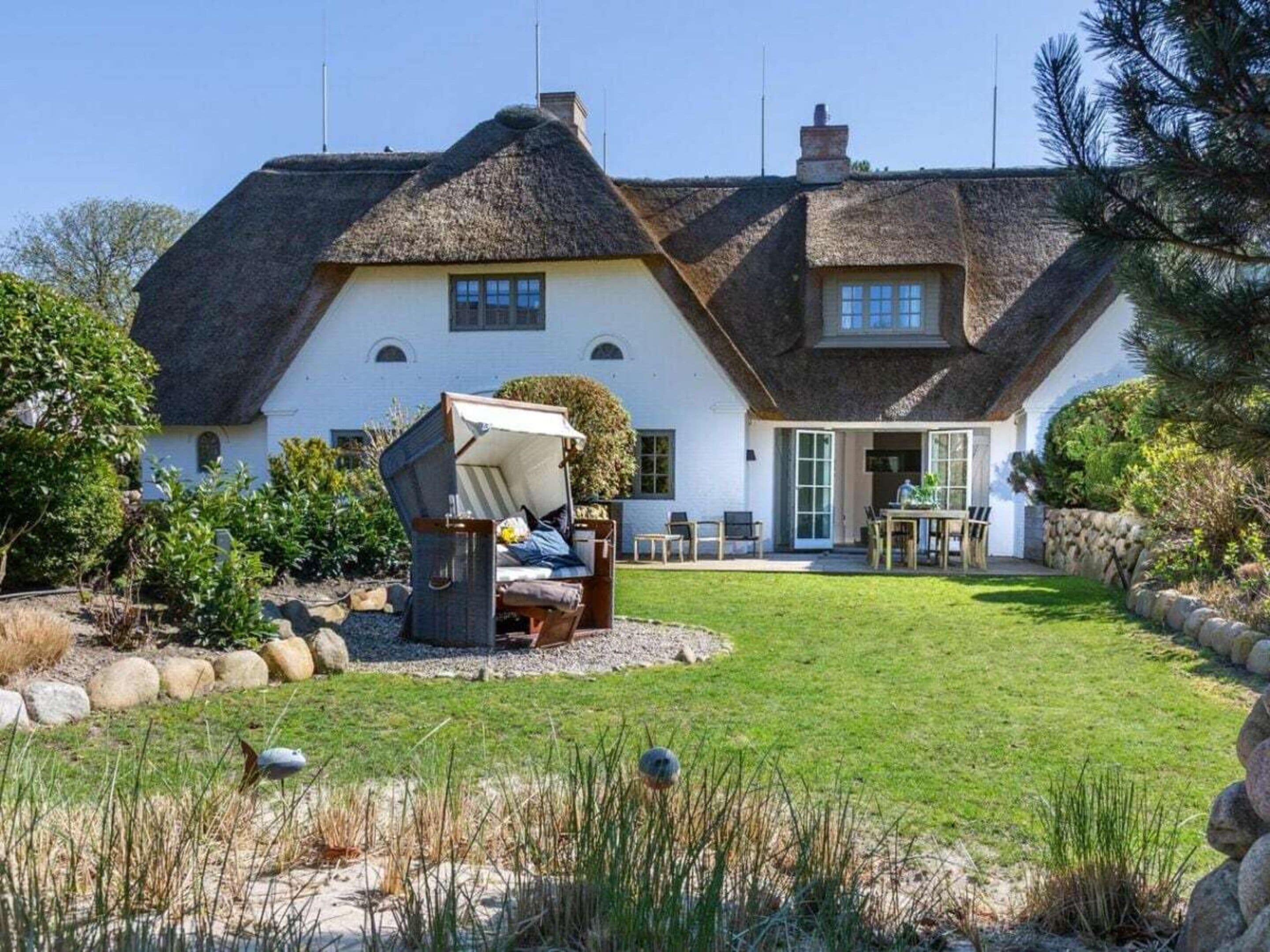 A house with a thatched roof, a garden with a swing set, and a stone wall.