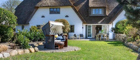 A house with a thatched roof, a garden with a swing set, and a stone wall.