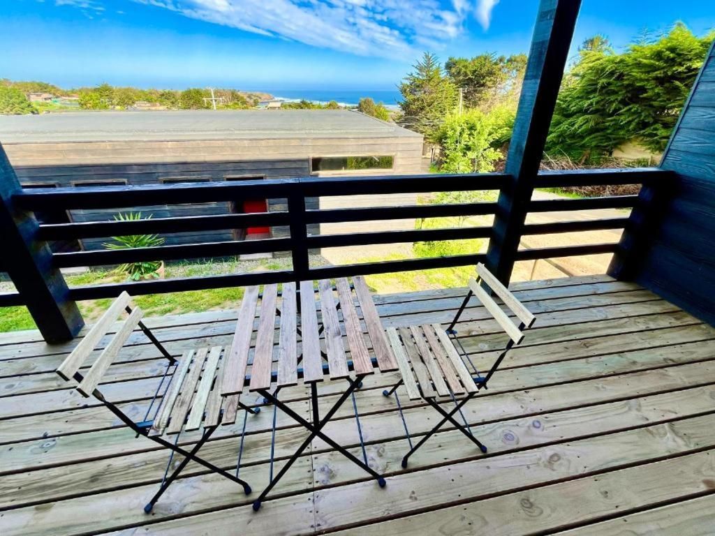 A wooden deck with a table and chairs, overlooking a view of the ocean and greenery.