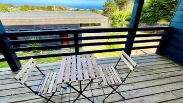 A wooden deck with a table and chairs, overlooking a view of the ocean and greenery.