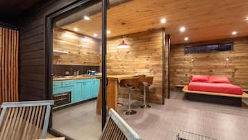 A modern interior with a wooden ceiling, a kitchen area, a dining space with stools, and a bed with red bedding.