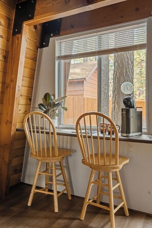 A wooden interior with two wooden chairs at a window, a coffee maker, and a thermometer on the window sill. - Enchanting 2BR Cabin with Private Spa • Big Bear Getaway (Big Bear)