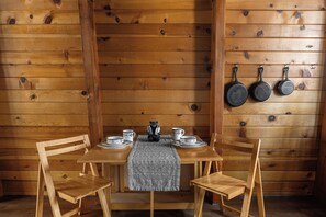 Un intérieur en bois avec une table à manger dressée pour deux personnes, des chaises, une figurine d’ours et des ustensiles de cuisine accrochés au mur.