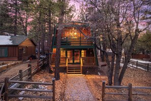 A cabin with a wooden deck and a covered porch, surrounded by trees and a gravel path. - Enchanting 2BR Cabin with Private Spa • Big Bear Getaway (Big Bear)