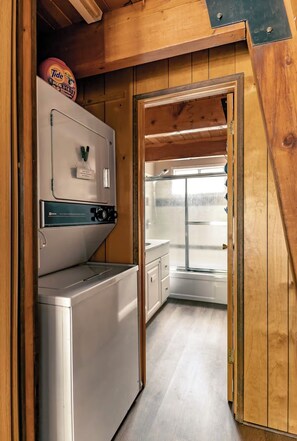 Une cuisine compacte équipée d’un lave-linge, d’un petit réfrigérateur et d’une porte en verre donnant sur un espace douche.