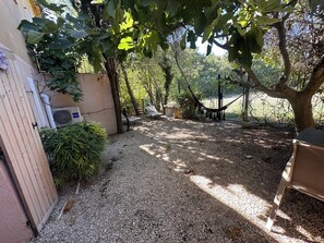 A gravel patio with a hammock, a wooden gate, and a fenced area with trees.