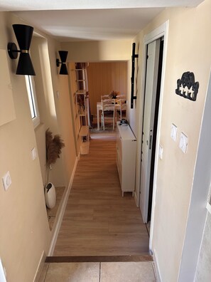 A hallway with a wooden floor, a white bench, a dining table with chairs, and a black wall-mounted light fixture.