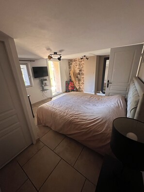 A bedroom with a large bed, a flat-screen TV mounted on the wall, a stone accent wall, and a door leading to another room.