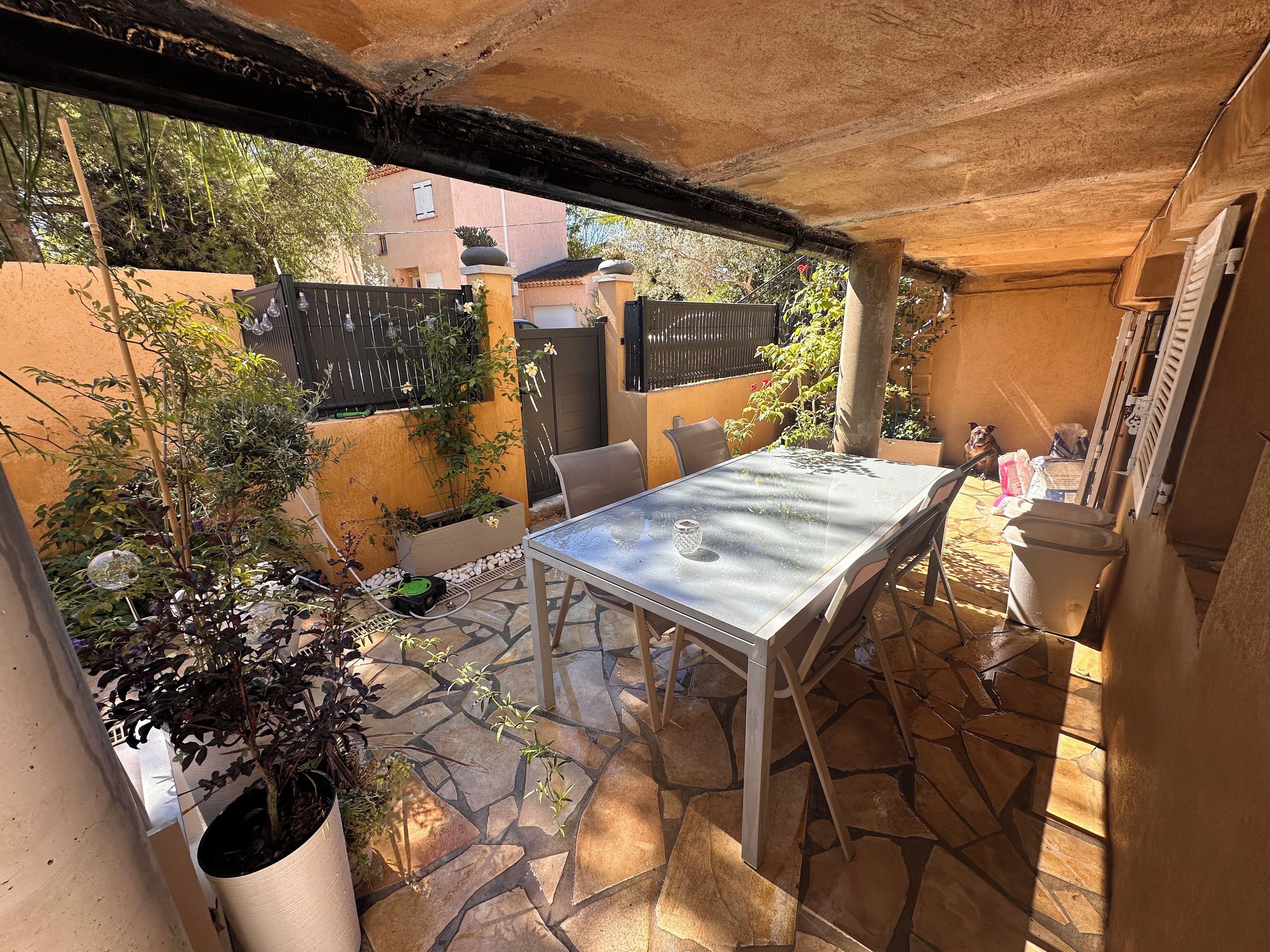 An outdoor patio with a table and chairs, surrounded by potted plants and a stone floor.