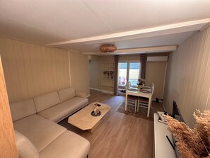 A living room with a beige sofa, a coffee table, and a dining area with a white table and chairs.