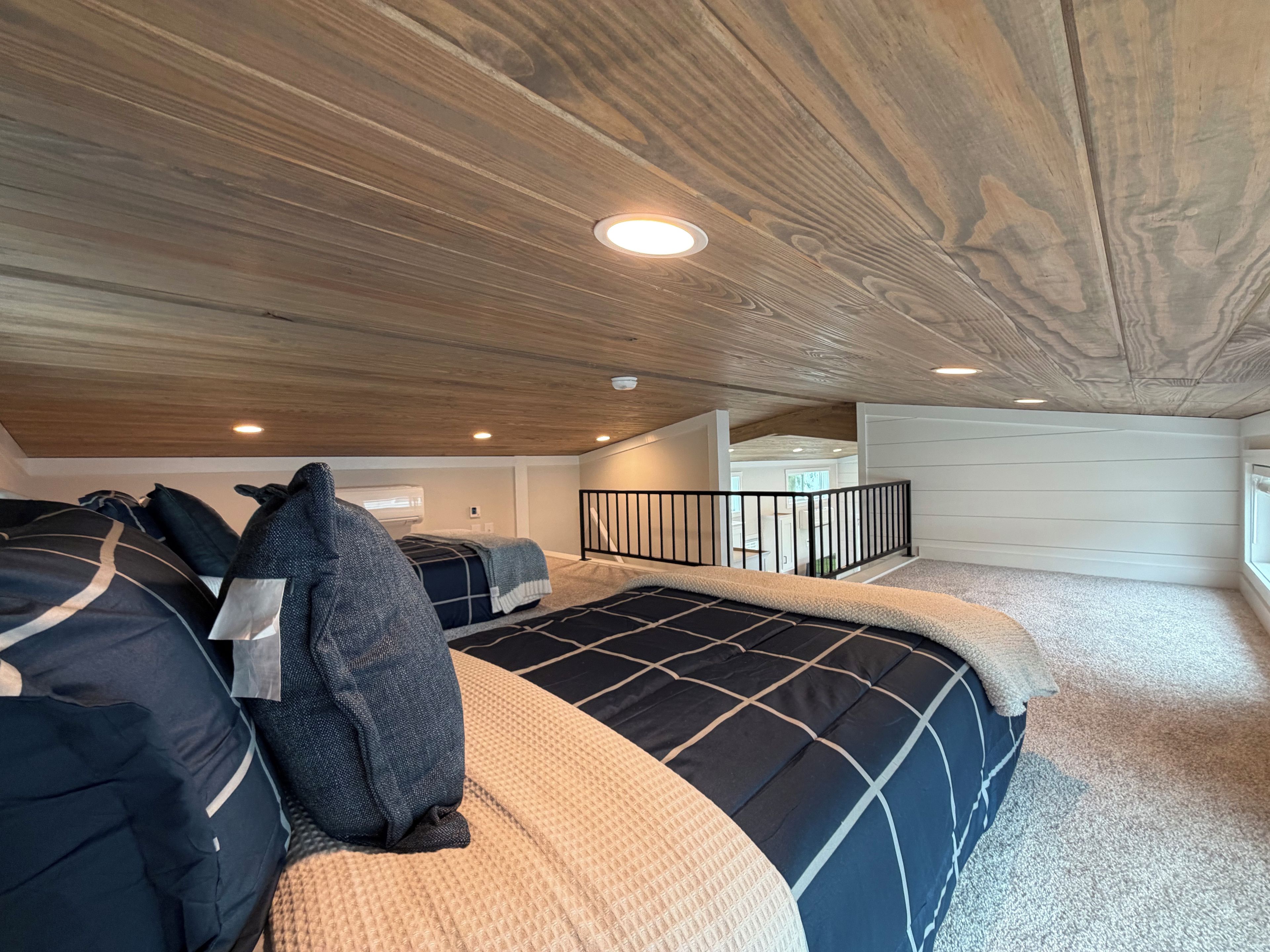 Una camera da letto con soffitto in legno, un letto con copriletto decorato, una finestra e vista su un'altra stanza.