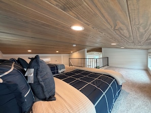 Une chambre avec un plafond en bois, un lit avec une literie à motifs, une fenêtre et une vue sur une autre pièce.