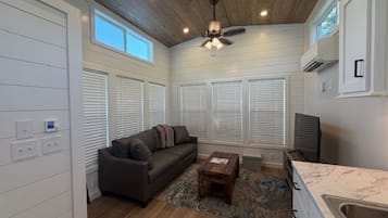 A living room with a ceiling fan, a sofa, a coffee table, and a kitchen area with a sink.
