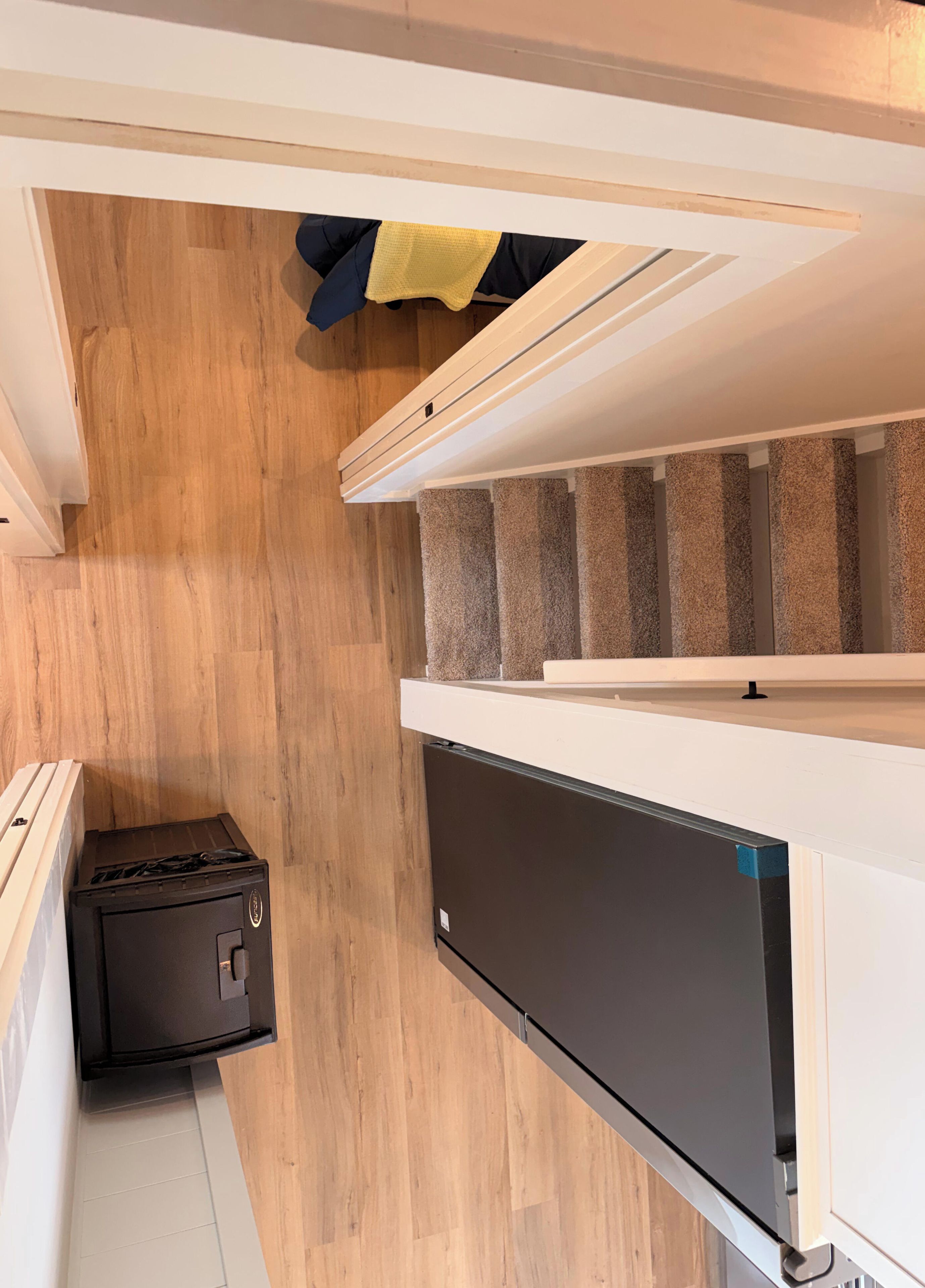 A compact kitchen with a built-in dishwasher, a wooden floor, and a staircase with beige carpeting.