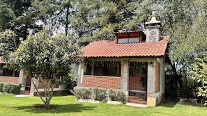 A small brick house with a tiled roof, surrounded by greenery.