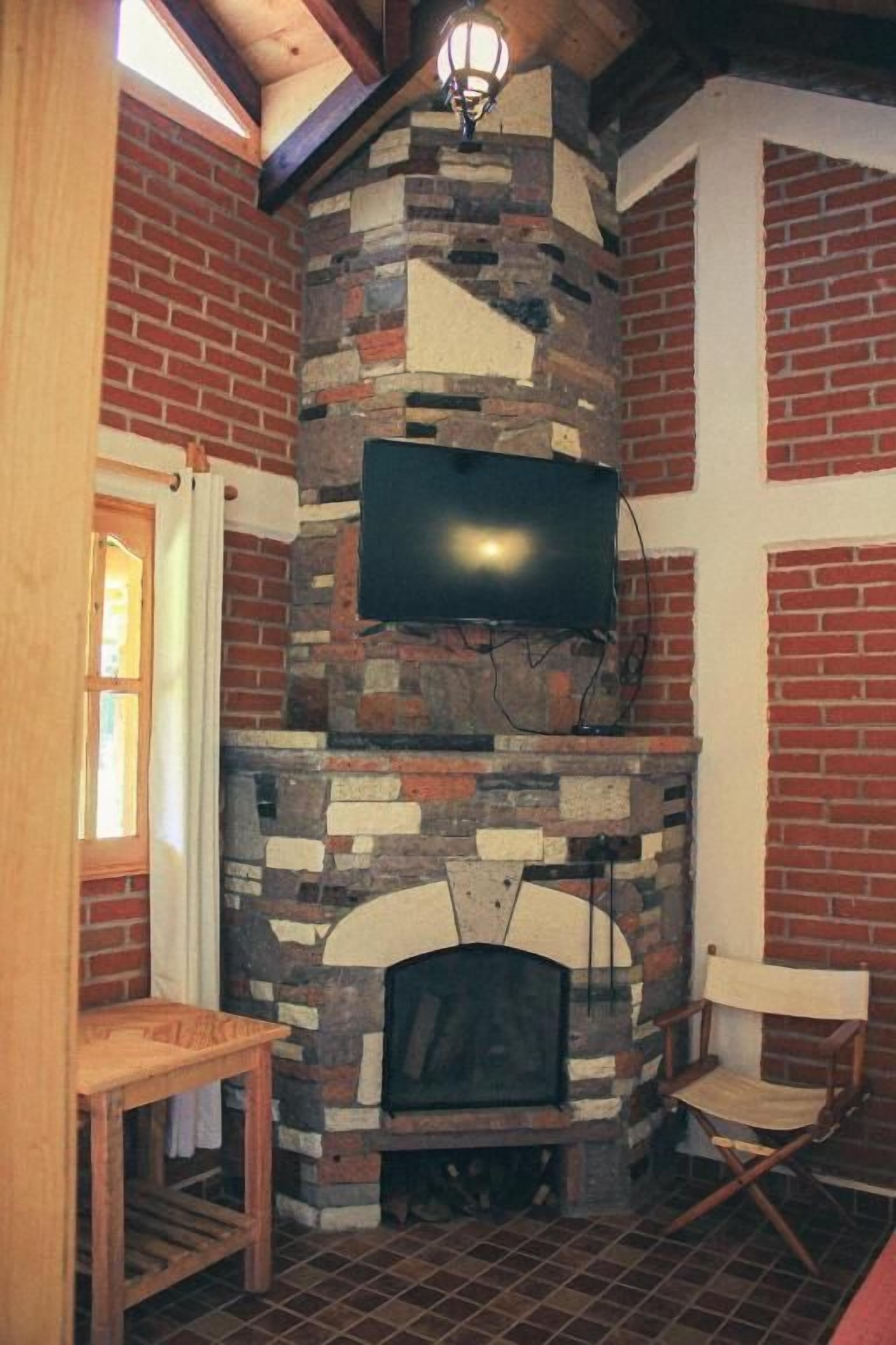 A stone fireplace with a television mounted above it, a wooden bench, and a chair.