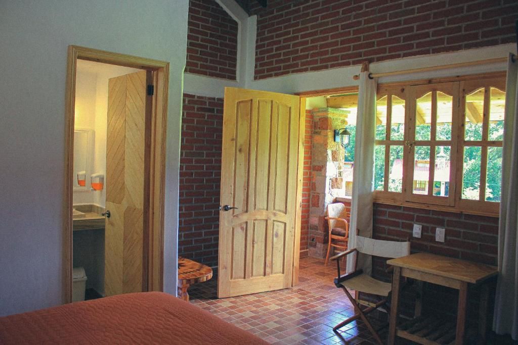 A room with a wooden door, a small table, a chair, and a window with a view of greenery.