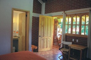 A room with a wooden door, a small table, a chair, and a window with a view of greenery. - Cabañas Rincón Escondido By GEstores (Huasca De Ocampo)
