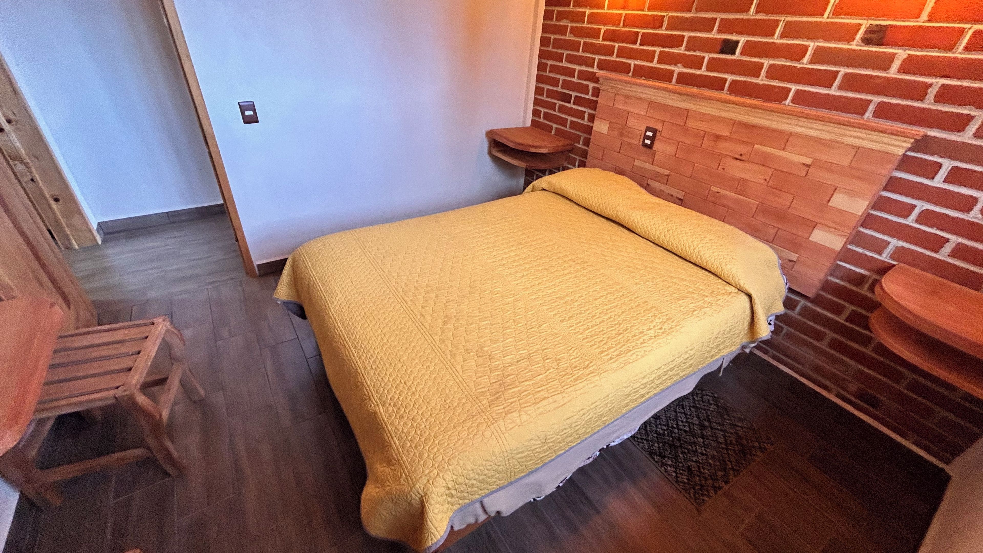 A bedroom with a bed, a wooden bench, a brick fireplace, and a door.