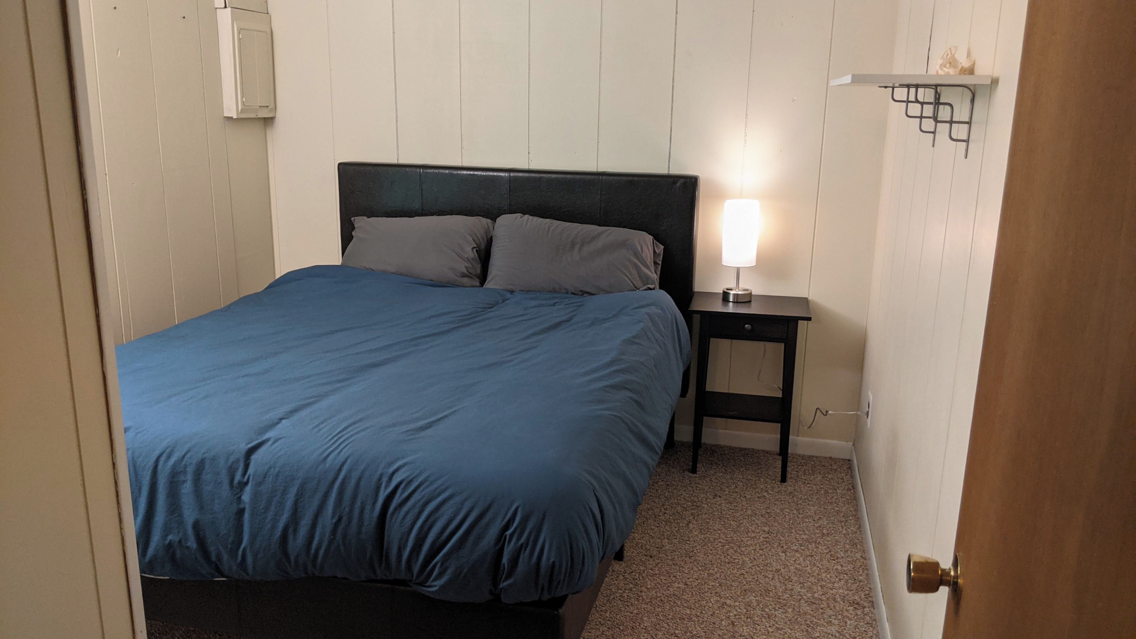 Une chambre à coucher avec un lit, une table de chevet avec une lampe et une porte.