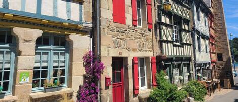 A traditional European street with half-timbered buildings, a red door, and a sign indicating a Gîte accommodation.