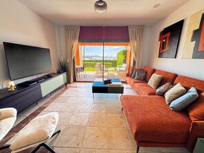 A modern living room with a flat-screen TV, a sofa, a coffee table, and a dining area with outdoor seating. - Beautiful modern Apartment with GYM (Estepona)