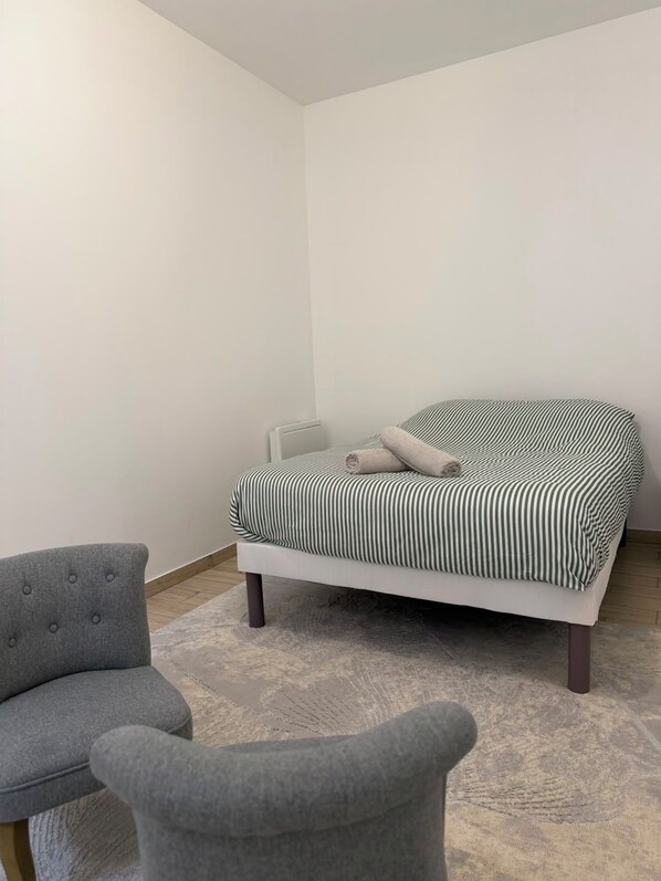 A room with a bed, a grey upholstered chair, and a radiator.