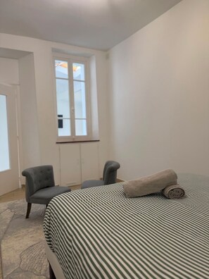 A bedroom with a bed, two chairs, a window, and a door.